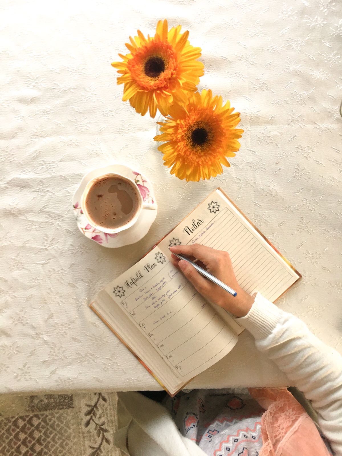 An open planner beside flowers and a drink